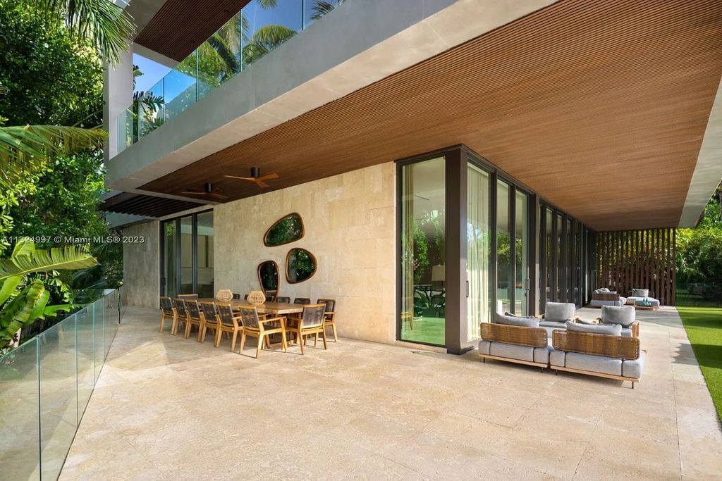 28 W Di Lido Drive, Miami Beach, Florida is stunning home where relaxed island living meets worldly sophistication, incredible features include 12ft ceilings, column-free living, 54ft of automated glass, media bookshelf, wine bar, & vapor fireplace highlight the textured travertine and white oak palette.