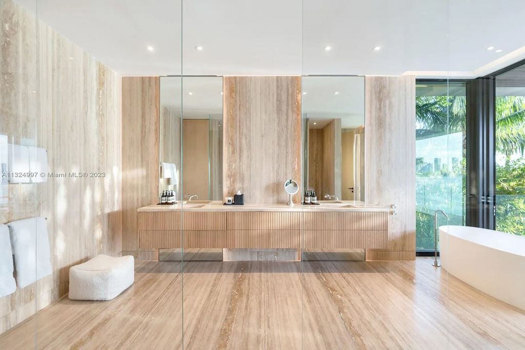 28 W Di Lido Drive, Miami Beach, Florida is stunning home where relaxed island living meets worldly sophistication, incredible features include 12ft ceilings, column-free living, 54ft of automated glass, media bookshelf, wine bar, & vapor fireplace highlight the textured travertine and white oak palette.
