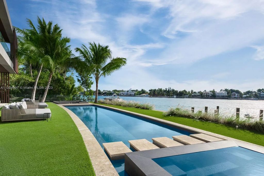 28 W Di Lido Drive, Miami Beach, Florida is stunning home where relaxed island living meets worldly sophistication, incredible features include 12ft ceilings, column-free living, 54ft of automated glass, media bookshelf, wine bar, & vapor fireplace highlight the textured travertine and white oak palette.