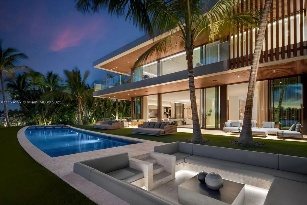 28 W Di Lido Drive, Miami Beach, Florida is stunning home where relaxed island living meets worldly sophistication, incredible features include 12ft ceilings, column-free living, 54ft of automated glass, media bookshelf, wine bar, & vapor fireplace highlight the textured travertine and white oak palette.