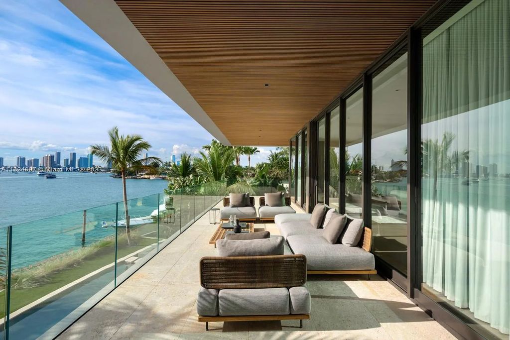 28 W Di Lido Drive, Miami Beach, Florida is stunning home where relaxed island living meets worldly sophistication, incredible features include 12ft ceilings, column-free living, 54ft of automated glass, media bookshelf, wine bar, & vapor fireplace highlight the textured travertine and white oak palette.