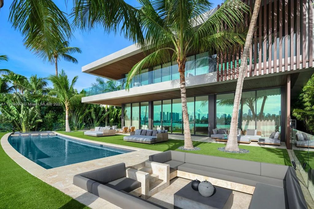 28 W Di Lido Drive, Miami Beach, Florida is stunning home where relaxed island living meets worldly sophistication, incredible features include 12ft ceilings, column-free living, 54ft of automated glass, media bookshelf, wine bar, & vapor fireplace highlight the textured travertine and white oak palette.