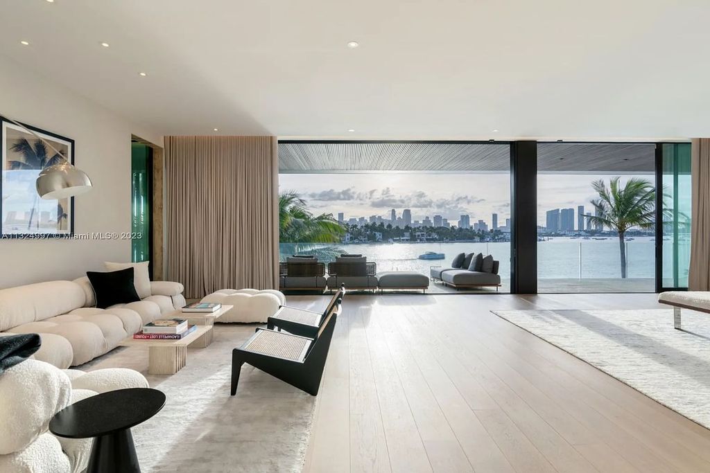 28 W Di Lido Drive, Miami Beach, Florida is stunning home where relaxed island living meets worldly sophistication, incredible features include 12ft ceilings, column-free living, 54ft of automated glass, media bookshelf, wine bar, & vapor fireplace highlight the textured travertine and white oak palette.