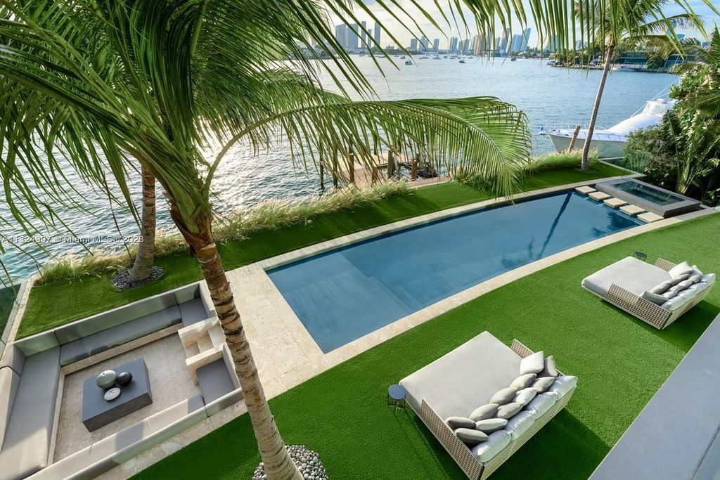 28 W Di Lido Drive, Miami Beach, Florida is stunning home where relaxed island living meets worldly sophistication, incredible features include 12ft ceilings, column-free living, 54ft of automated glass, media bookshelf, wine bar, & vapor fireplace highlight the textured travertine and white oak palette.