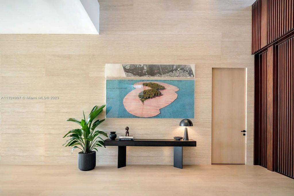 28 W Di Lido Drive, Miami Beach, Florida is stunning home where relaxed island living meets worldly sophistication, incredible features include 12ft ceilings, column-free living, 54ft of automated glass, media bookshelf, wine bar, & vapor fireplace highlight the textured travertine and white oak palette.