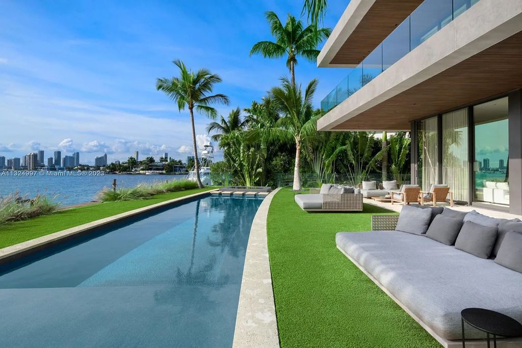 28 W Di Lido Drive, Miami Beach, Florida is stunning home where relaxed island living meets worldly sophistication, incredible features include 12ft ceilings, column-free living, 54ft of automated glass, media bookshelf, wine bar, & vapor fireplace highlight the textured travertine and white oak palette.