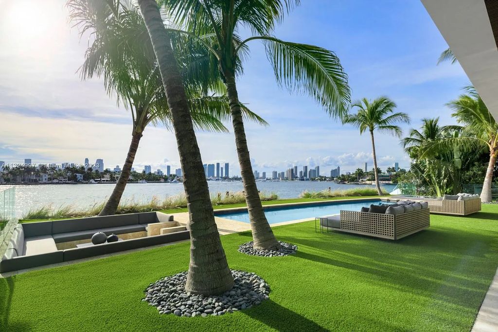 28 W Di Lido Drive, Miami Beach, Florida is stunning home where relaxed island living meets worldly sophistication, incredible features include 12ft ceilings, column-free living, 54ft of automated glass, media bookshelf, wine bar, & vapor fireplace highlight the textured travertine and white oak palette.