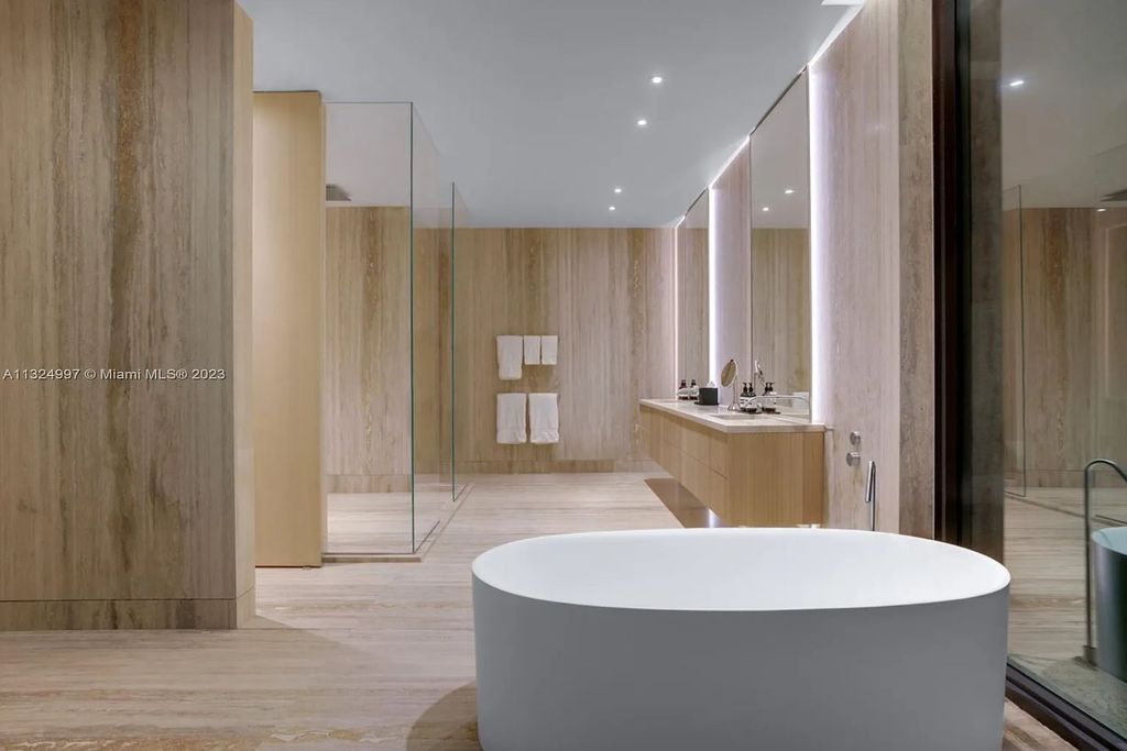 28 W Di Lido Drive, Miami Beach, Florida is stunning home where relaxed island living meets worldly sophistication, incredible features include 12ft ceilings, column-free living, 54ft of automated glass, media bookshelf, wine bar, & vapor fireplace highlight the textured travertine and white oak palette.