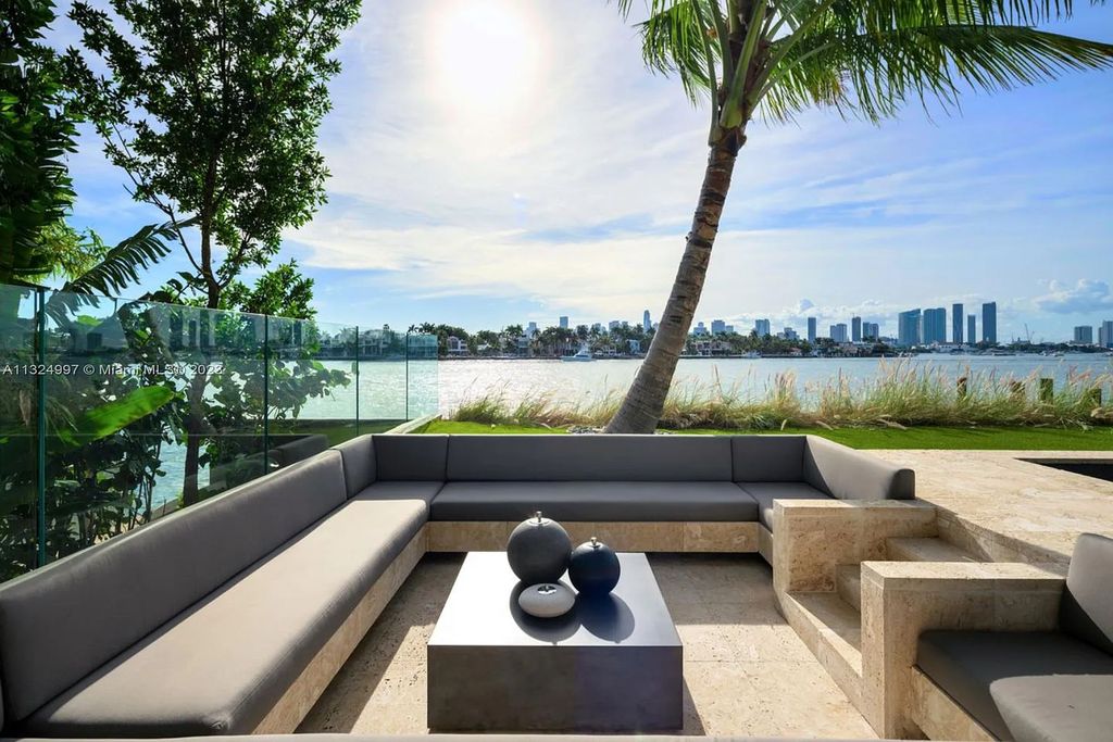 28 W Di Lido Drive, Miami Beach, Florida is stunning home where relaxed island living meets worldly sophistication, incredible features include 12ft ceilings, column-free living, 54ft of automated glass, media bookshelf, wine bar, & vapor fireplace highlight the textured travertine and white oak palette.