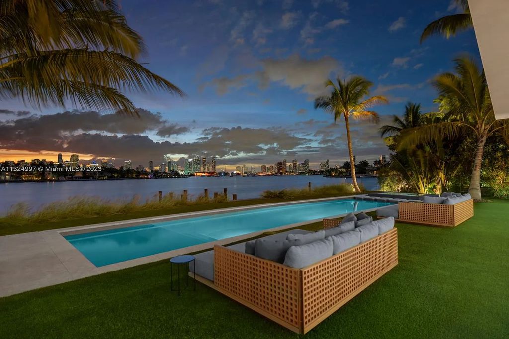 28 W Di Lido Drive, Miami Beach, Florida is stunning home where relaxed island living meets worldly sophistication, incredible features include 12ft ceilings, column-free living, 54ft of automated glass, media bookshelf, wine bar, & vapor fireplace highlight the textured travertine and white oak palette.