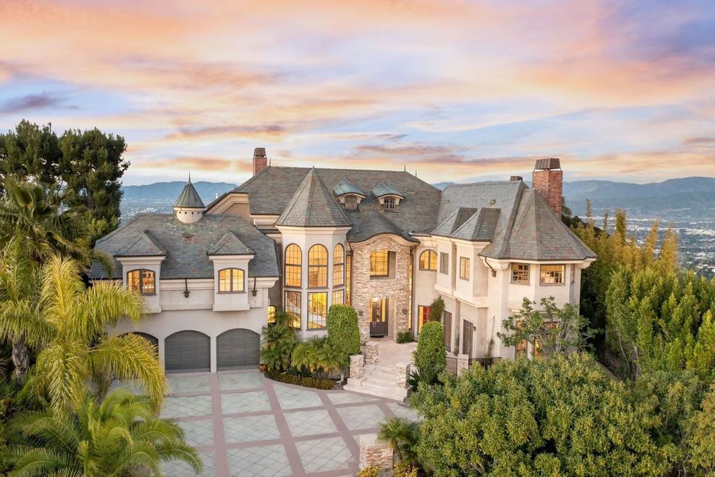This exquisite estate offers breathtaking 360-degree views of the ocean sunsets, city lights, and Santa Monica mountains skyline, visible from its three stunning balconies. With over 9,300 square feet of space, this luxurious property boasts five bedrooms, seven bathrooms, three living rooms, formal and informal dining areas, and five beautiful fireplaces. The grand entrance through double doors leads to a dramatic 2-story foyer with 30-foot windows that flood the space with natural light, and limestone floors create an elegant touch.