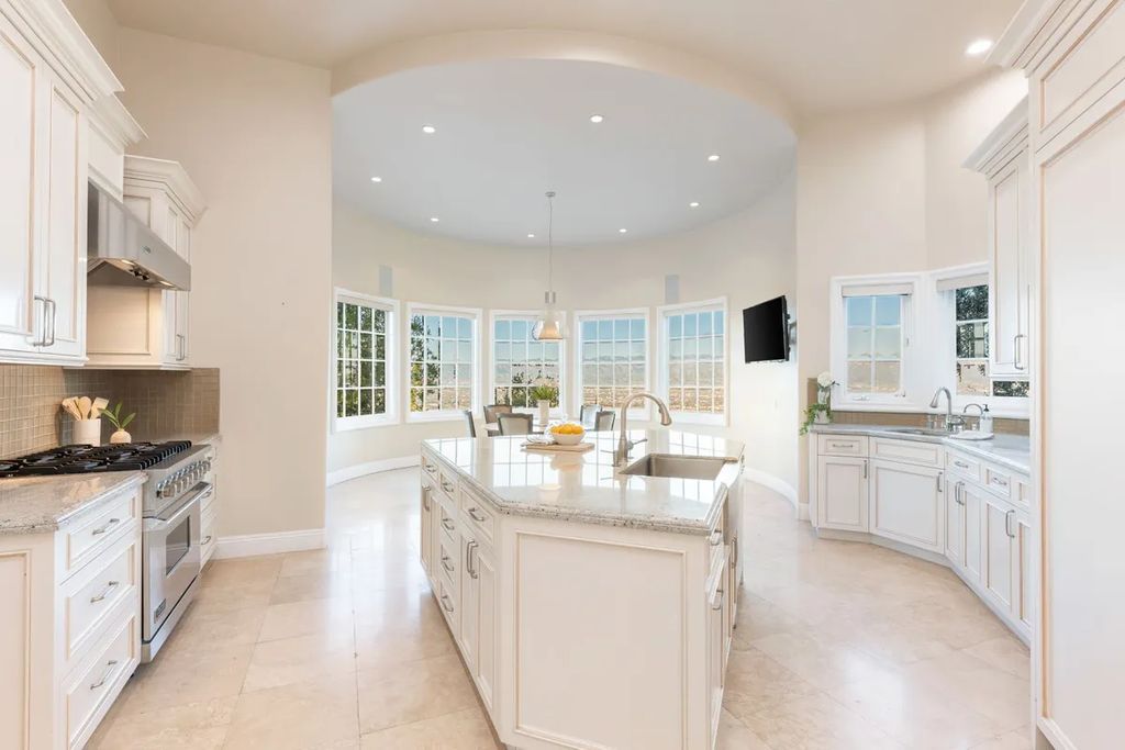 This exquisite estate offers breathtaking 360-degree views of the ocean sunsets, city lights, and Santa Monica mountains skyline, visible from its three stunning balconies. With over 9,300 square feet of space, this luxurious property boasts five bedrooms, seven bathrooms, three living rooms, formal and informal dining areas, and five beautiful fireplaces. The grand entrance through double doors leads to a dramatic 2-story foyer with 30-foot windows that flood the space with natural light, and limestone floors create an elegant touch.