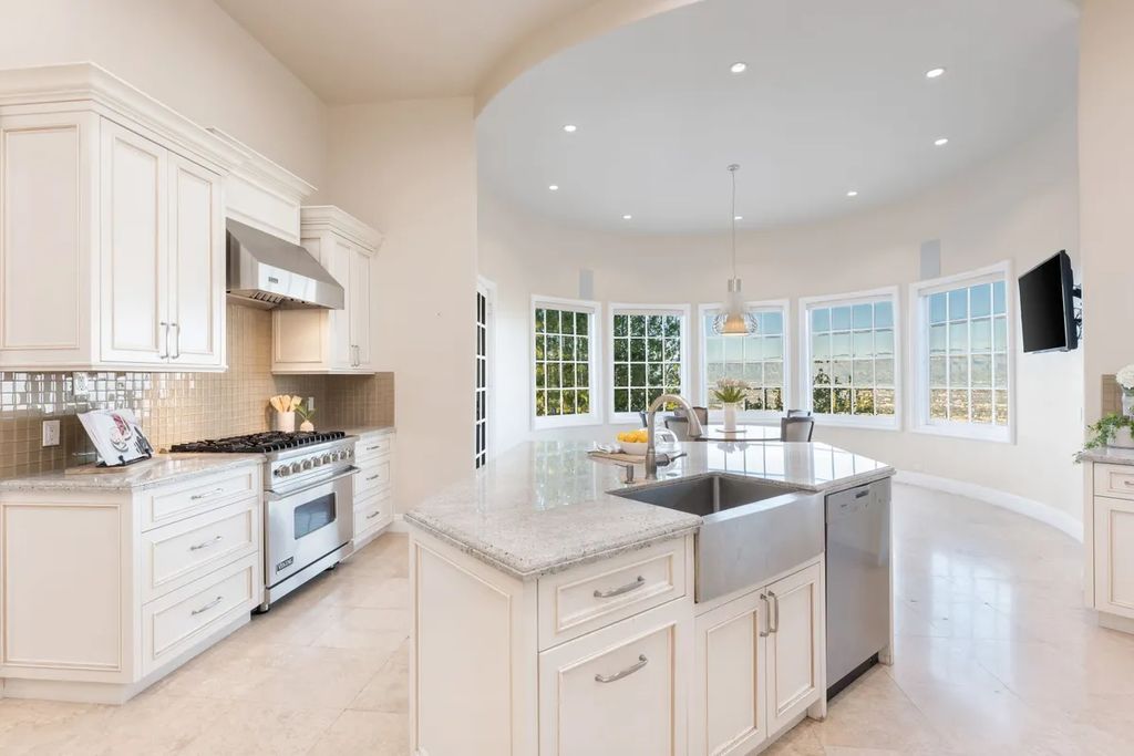 This exquisite estate offers breathtaking 360-degree views of the ocean sunsets, city lights, and Santa Monica mountains skyline, visible from its three stunning balconies. With over 9,300 square feet of space, this luxurious property boasts five bedrooms, seven bathrooms, three living rooms, formal and informal dining areas, and five beautiful fireplaces. The grand entrance through double doors leads to a dramatic 2-story foyer with 30-foot windows that flood the space with natural light, and limestone floors create an elegant touch.