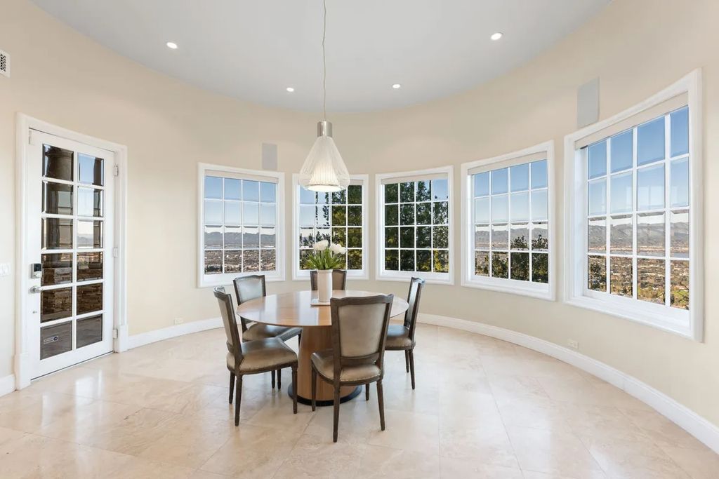 This exquisite estate offers breathtaking 360-degree views of the ocean sunsets, city lights, and Santa Monica mountains skyline, visible from its three stunning balconies. With over 9,300 square feet of space, this luxurious property boasts five bedrooms, seven bathrooms, three living rooms, formal and informal dining areas, and five beautiful fireplaces. The grand entrance through double doors leads to a dramatic 2-story foyer with 30-foot windows that flood the space with natural light, and limestone floors create an elegant touch.