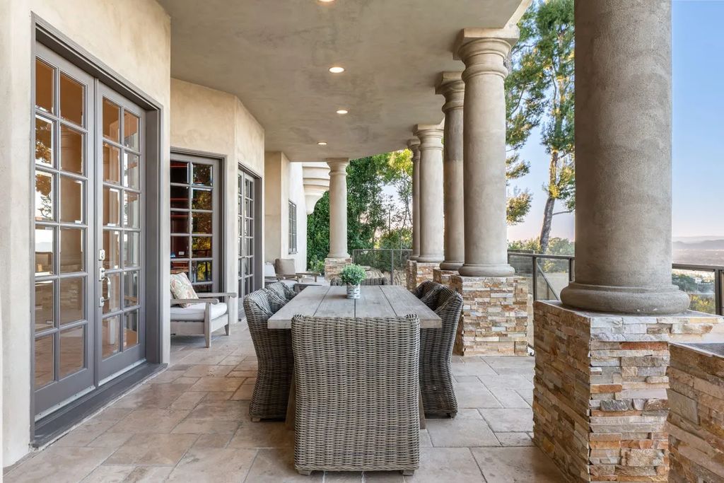 This exquisite estate offers breathtaking 360-degree views of the ocean sunsets, city lights, and Santa Monica mountains skyline, visible from its three stunning balconies. With over 9,300 square feet of space, this luxurious property boasts five bedrooms, seven bathrooms, three living rooms, formal and informal dining areas, and five beautiful fireplaces. The grand entrance through double doors leads to a dramatic 2-story foyer with 30-foot windows that flood the space with natural light, and limestone floors create an elegant touch.
