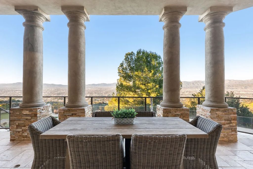 This exquisite estate offers breathtaking 360-degree views of the ocean sunsets, city lights, and Santa Monica mountains skyline, visible from its three stunning balconies. With over 9,300 square feet of space, this luxurious property boasts five bedrooms, seven bathrooms, three living rooms, formal and informal dining areas, and five beautiful fireplaces. The grand entrance through double doors leads to a dramatic 2-story foyer with 30-foot windows that flood the space with natural light, and limestone floors create an elegant touch.