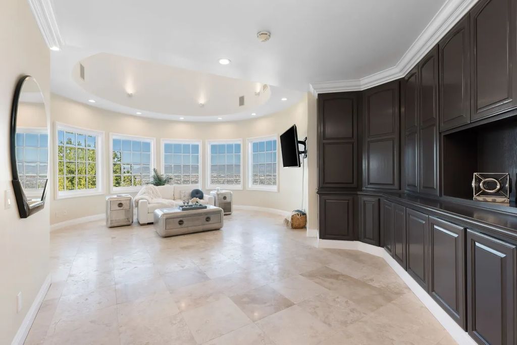 This exquisite estate offers breathtaking 360-degree views of the ocean sunsets, city lights, and Santa Monica mountains skyline, visible from its three stunning balconies. With over 9,300 square feet of space, this luxurious property boasts five bedrooms, seven bathrooms, three living rooms, formal and informal dining areas, and five beautiful fireplaces. The grand entrance through double doors leads to a dramatic 2-story foyer with 30-foot windows that flood the space with natural light, and limestone floors create an elegant touch.