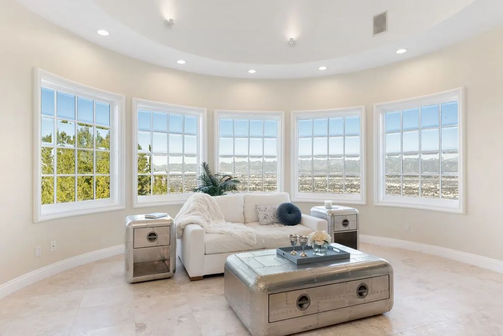 This exquisite estate offers breathtaking 360-degree views of the ocean sunsets, city lights, and Santa Monica mountains skyline, visible from its three stunning balconies. With over 9,300 square feet of space, this luxurious property boasts five bedrooms, seven bathrooms, three living rooms, formal and informal dining areas, and five beautiful fireplaces. The grand entrance through double doors leads to a dramatic 2-story foyer with 30-foot windows that flood the space with natural light, and limestone floors create an elegant touch.