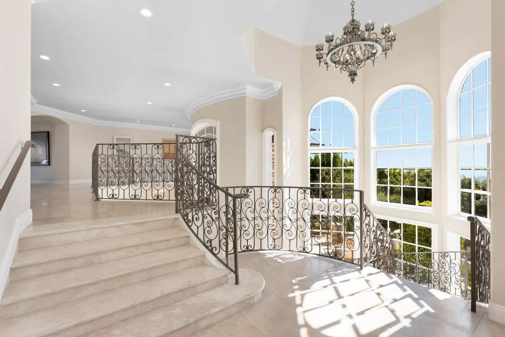 This exquisite estate offers breathtaking 360-degree views of the ocean sunsets, city lights, and Santa Monica mountains skyline, visible from its three stunning balconies. With over 9,300 square feet of space, this luxurious property boasts five bedrooms, seven bathrooms, three living rooms, formal and informal dining areas, and five beautiful fireplaces. The grand entrance through double doors leads to a dramatic 2-story foyer with 30-foot windows that flood the space with natural light, and limestone floors create an elegant touch.
