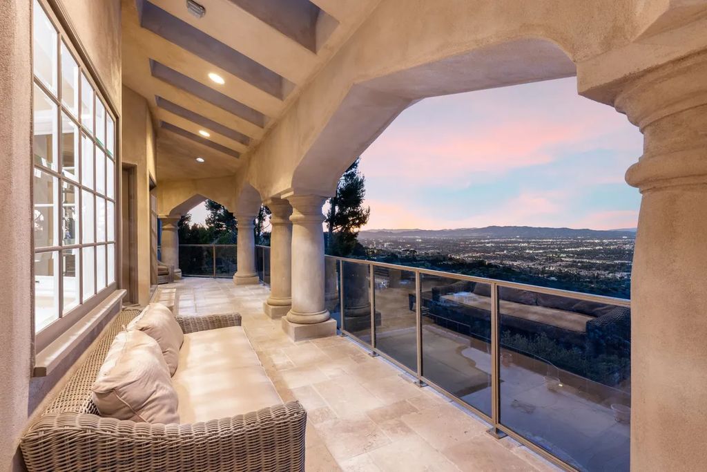 This exquisite estate offers breathtaking 360-degree views of the ocean sunsets, city lights, and Santa Monica mountains skyline, visible from its three stunning balconies. With over 9,300 square feet of space, this luxurious property boasts five bedrooms, seven bathrooms, three living rooms, formal and informal dining areas, and five beautiful fireplaces. The grand entrance through double doors leads to a dramatic 2-story foyer with 30-foot windows that flood the space with natural light, and limestone floors create an elegant touch.
