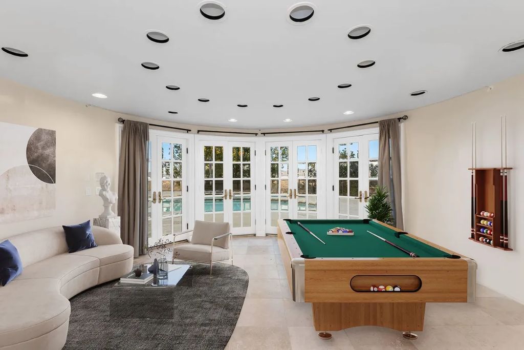 This exquisite estate offers breathtaking 360-degree views of the ocean sunsets, city lights, and Santa Monica mountains skyline, visible from its three stunning balconies. With over 9,300 square feet of space, this luxurious property boasts five bedrooms, seven bathrooms, three living rooms, formal and informal dining areas, and five beautiful fireplaces. The grand entrance through double doors leads to a dramatic 2-story foyer with 30-foot windows that flood the space with natural light, and limestone floors create an elegant touch.