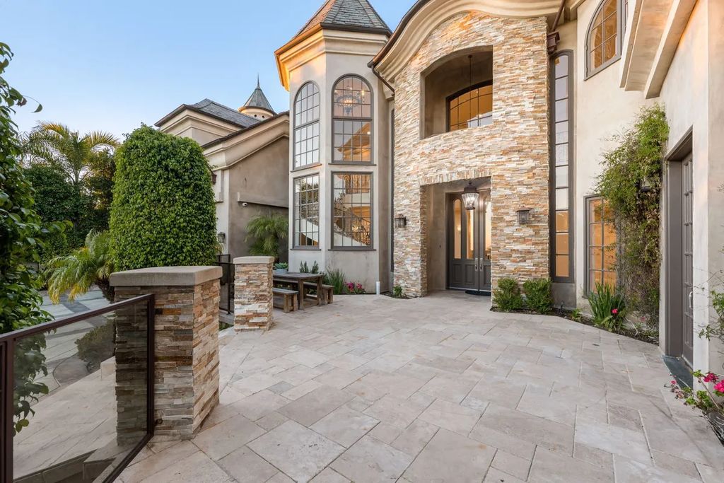 This exquisite estate offers breathtaking 360-degree views of the ocean sunsets, city lights, and Santa Monica mountains skyline, visible from its three stunning balconies. With over 9,300 square feet of space, this luxurious property boasts five bedrooms, seven bathrooms, three living rooms, formal and informal dining areas, and five beautiful fireplaces. The grand entrance through double doors leads to a dramatic 2-story foyer with 30-foot windows that flood the space with natural light, and limestone floors create an elegant touch.