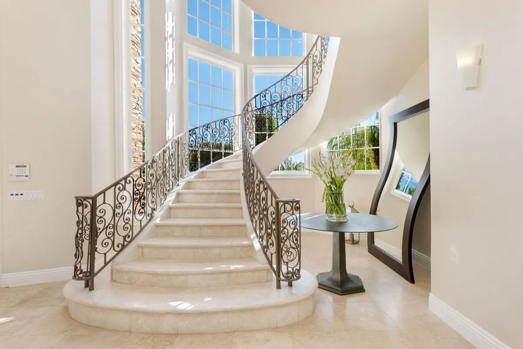 This exquisite estate offers breathtaking 360-degree views of the ocean sunsets, city lights, and Santa Monica mountains skyline, visible from its three stunning balconies. With over 9,300 square feet of space, this luxurious property boasts five bedrooms, seven bathrooms, three living rooms, formal and informal dining areas, and five beautiful fireplaces. The grand entrance through double doors leads to a dramatic 2-story foyer with 30-foot windows that flood the space with natural light, and limestone floors create an elegant touch.