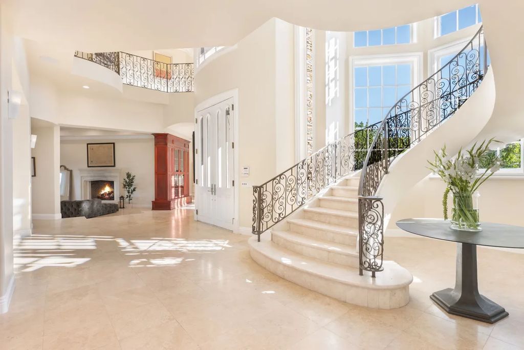 This exquisite estate offers breathtaking 360-degree views of the ocean sunsets, city lights, and Santa Monica mountains skyline, visible from its three stunning balconies. With over 9,300 square feet of space, this luxurious property boasts five bedrooms, seven bathrooms, three living rooms, formal and informal dining areas, and five beautiful fireplaces. The grand entrance through double doors leads to a dramatic 2-story foyer with 30-foot windows that flood the space with natural light, and limestone floors create an elegant touch.