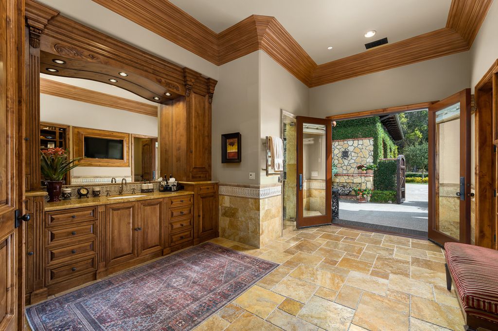 Indulge in the lavishness of a sprawling Mediterranean estate located on 4.71 acres in the sought-after Rancho Santa Fe. This private gated property boasts a grand Tuscan villa with a circular drive featuring a serene fountain and four separate stone and vine-covered structures surrounded by lush greenery.