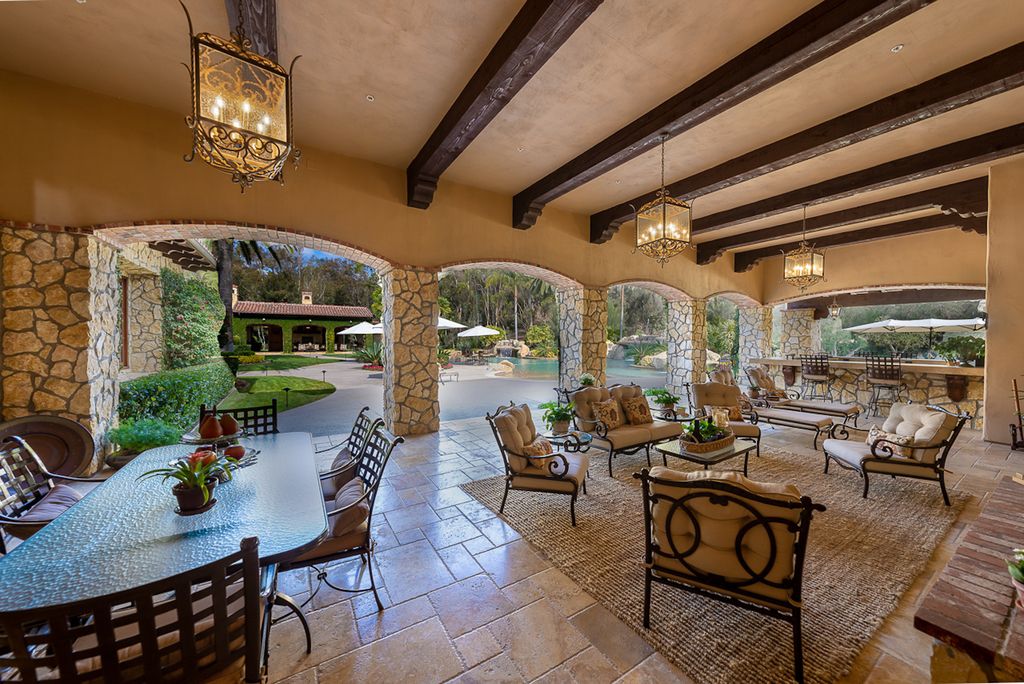 Indulge in the lavishness of a sprawling Mediterranean estate located on 4.71 acres in the sought-after Rancho Santa Fe. This private gated property boasts a grand Tuscan villa with a circular drive featuring a serene fountain and four separate stone and vine-covered structures surrounded by lush greenery.