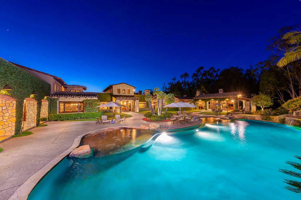 Indulge in the lavishness of a sprawling Mediterranean estate located on 4.71 acres in the sought-after Rancho Santa Fe. This private gated property boasts a grand Tuscan villa with a circular drive featuring a serene fountain and four separate stone and vine-covered structures surrounded by lush greenery.