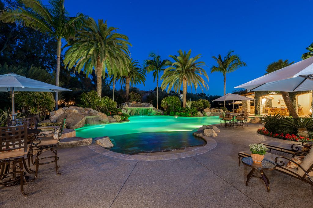 Indulge in the lavishness of a sprawling Mediterranean estate located on 4.71 acres in the sought-after Rancho Santa Fe. This private gated property boasts a grand Tuscan villa with a circular drive featuring a serene fountain and four separate stone and vine-covered structures surrounded by lush greenery.