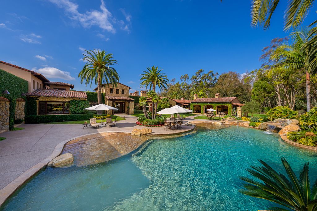 Indulge in the lavishness of a sprawling Mediterranean estate located on 4.71 acres in the sought-after Rancho Santa Fe. This private gated property boasts a grand Tuscan villa with a circular drive featuring a serene fountain and four separate stone and vine-covered structures surrounded by lush greenery.