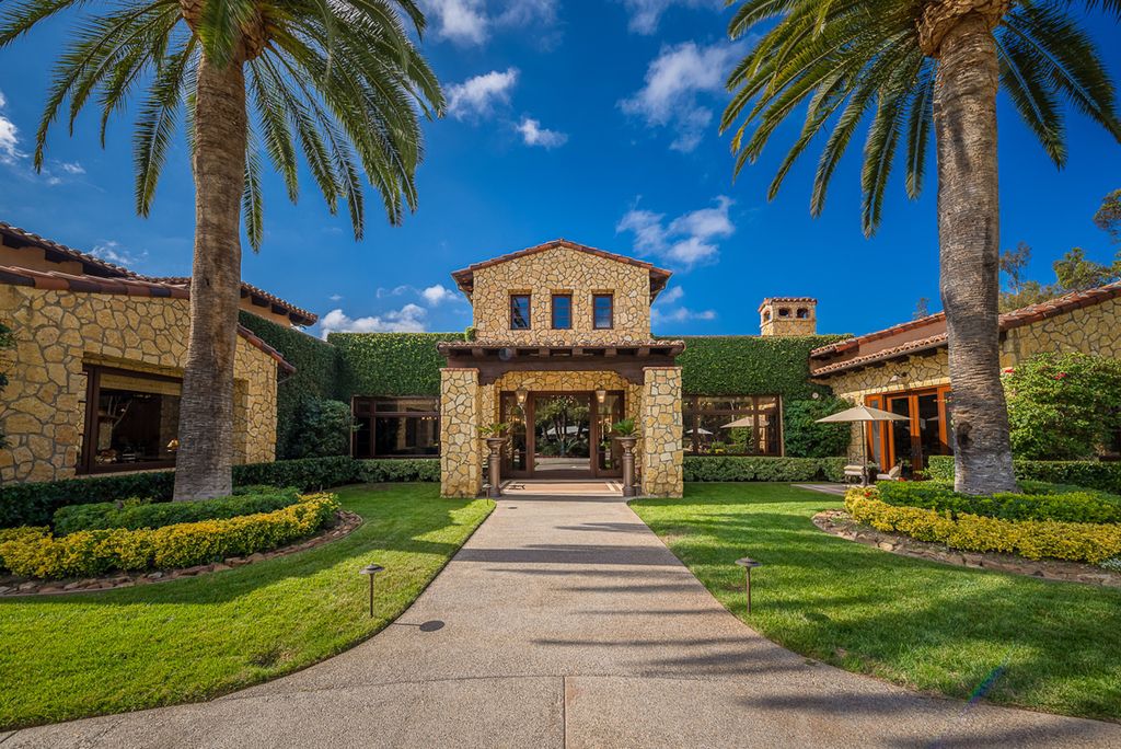 Indulge in the lavishness of a sprawling Mediterranean estate located on 4.71 acres in the sought-after Rancho Santa Fe. This private gated property boasts a grand Tuscan villa with a circular drive featuring a serene fountain and four separate stone and vine-covered structures surrounded by lush greenery.