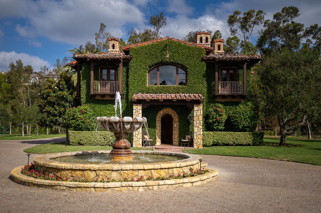 Indulge in the lavishness of a sprawling Mediterranean estate located on 4.71 acres in the sought-after Rancho Santa Fe. This private gated property boasts a grand Tuscan villa with a circular drive featuring a serene fountain and four separate stone and vine-covered structures surrounded by lush greenery.