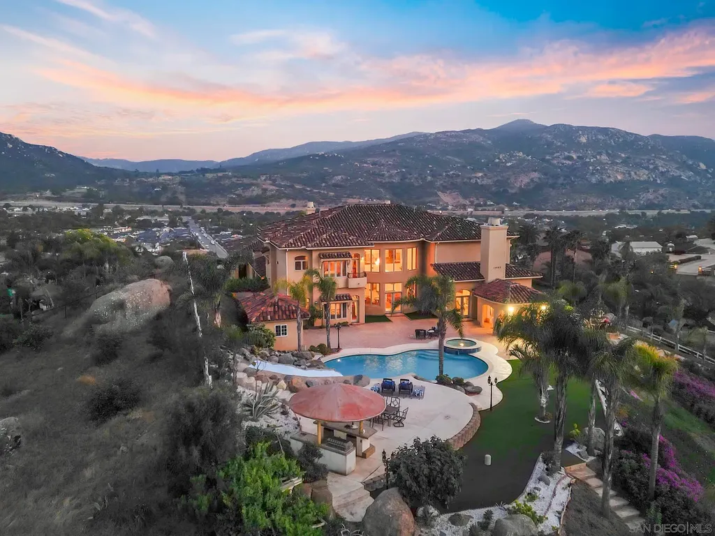 Elevated on a hill in Blossom Valley, this exquisite home offers a living experience that is truly unmatched. Nestled within a gated estate, the property expands across six acres of meticulously landscaped grounds, showcasing natural rock formations and a vibrant variety of palm trees, succulents, and blooming flowers. Embracing eco-friendly features such as a ground-water well and solar panels, this residence seamlessly blends sustainability with luxurious living. 15987 Broad Oaks Road Home in El Cajon, California.