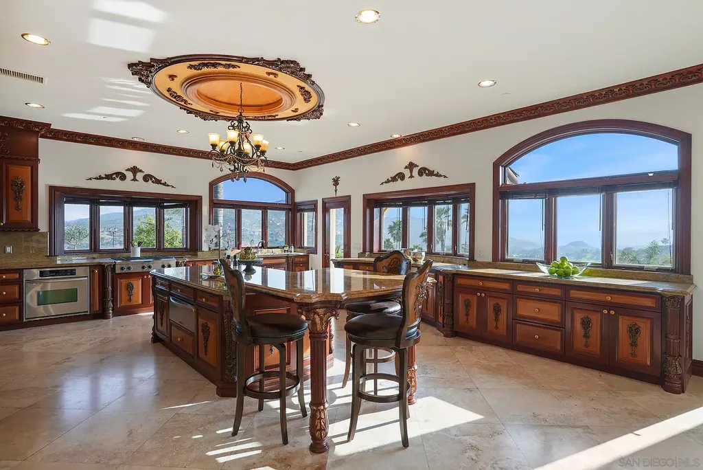 Elevated on a hill in Blossom Valley, this exquisite home offers a living experience that is truly unmatched. Nestled within a gated estate, the property expands across six acres of meticulously landscaped grounds, showcasing natural rock formations and a vibrant variety of palm trees, succulents, and blooming flowers. Embracing eco-friendly features such as a ground-water well and solar panels, this residence seamlessly blends sustainability with luxurious living. 15987 Broad Oaks Road Home in El Cajon, California.
