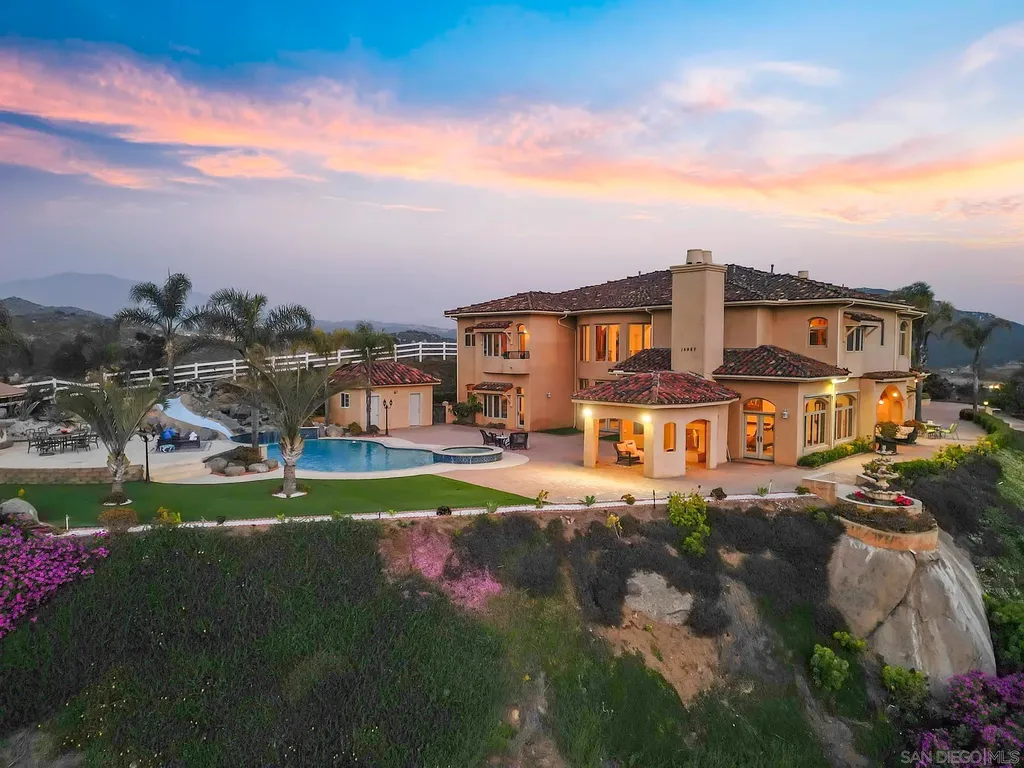Elevated on a hill in Blossom Valley, this exquisite home offers a living experience that is truly unmatched. Nestled within a gated estate, the property expands across six acres of meticulously landscaped grounds, showcasing natural rock formations and a vibrant variety of palm trees, succulents, and blooming flowers. Embracing eco-friendly features such as a ground-water well and solar panels, this residence seamlessly blends sustainability with luxurious living. 15987 Broad Oaks Road Home in El Cajon, California.