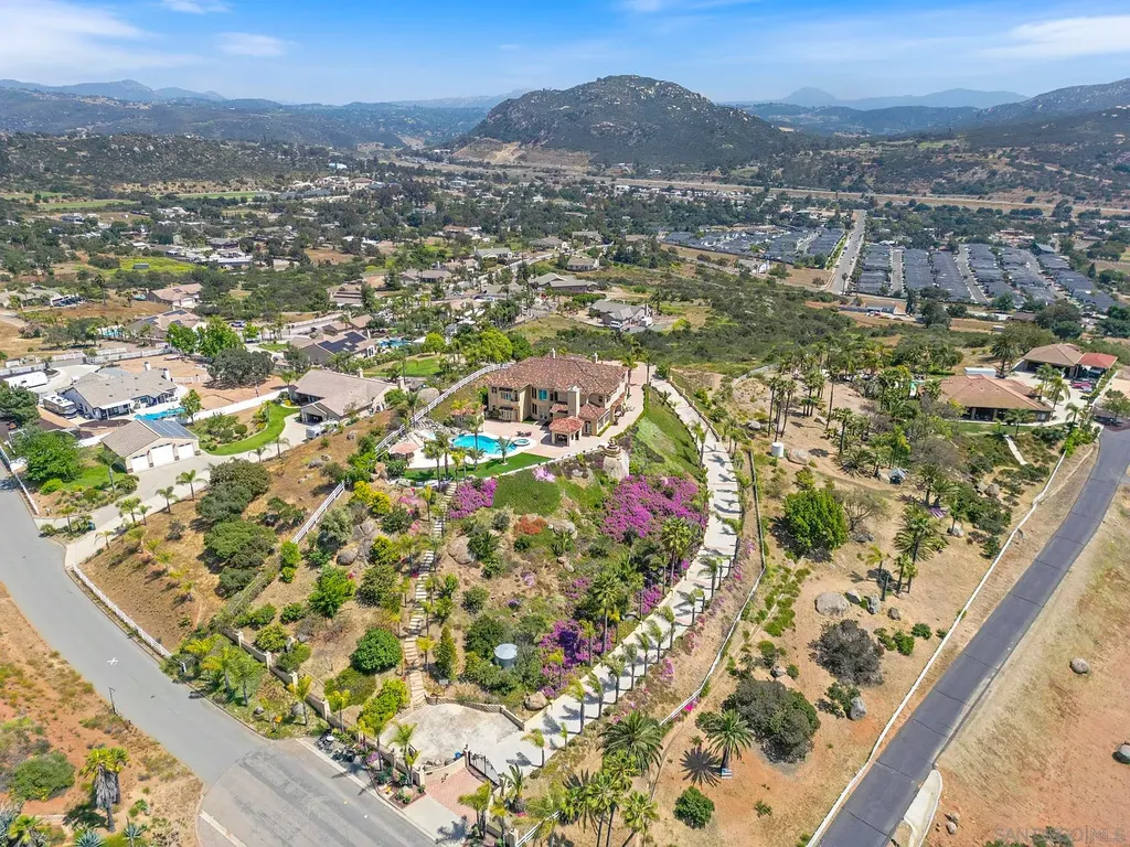 Elevated on a hill in Blossom Valley, this exquisite home offers a living experience that is truly unmatched. Nestled within a gated estate, the property expands across six acres of meticulously landscaped grounds, showcasing natural rock formations and a vibrant variety of palm trees, succulents, and blooming flowers. Embracing eco-friendly features such as a ground-water well and solar panels, this residence seamlessly blends sustainability with luxurious living. 15987 Broad Oaks Road Home in El Cajon, California.