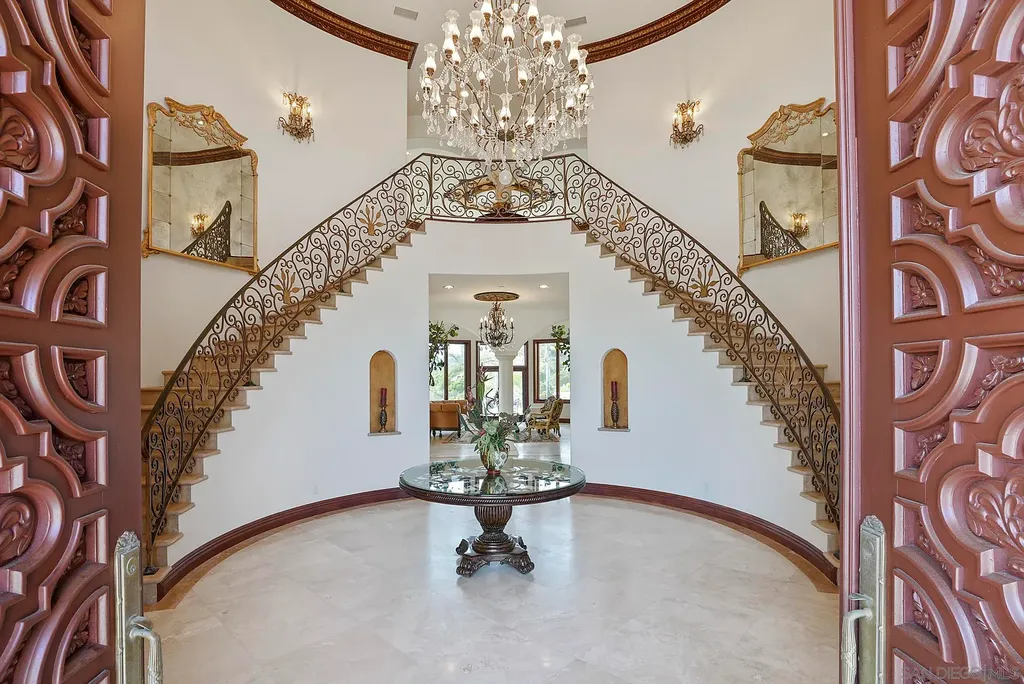 Elevated on a hill in Blossom Valley, this exquisite home offers a living experience that is truly unmatched. Nestled within a gated estate, the property expands across six acres of meticulously landscaped grounds, showcasing natural rock formations and a vibrant variety of palm trees, succulents, and blooming flowers. Embracing eco-friendly features such as a ground-water well and solar panels, this residence seamlessly blends sustainability with luxurious living. 15987 Broad Oaks Road Home in El Cajon, California.
