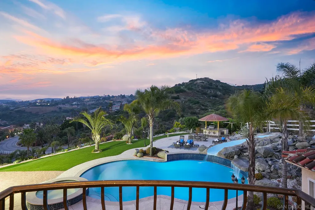 Elevated on a hill in Blossom Valley, this exquisite home offers a living experience that is truly unmatched. Nestled within a gated estate, the property expands across six acres of meticulously landscaped grounds, showcasing natural rock formations and a vibrant variety of palm trees, succulents, and blooming flowers. Embracing eco-friendly features such as a ground-water well and solar panels, this residence seamlessly blends sustainability with luxurious living. 15987 Broad Oaks Road Home in El Cajon, California.