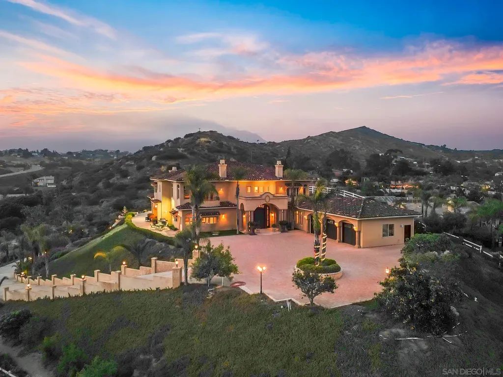 Elevated on a hill in Blossom Valley, this exquisite home offers a living experience that is truly unmatched. Nestled within a gated estate, the property expands across six acres of meticulously landscaped grounds, showcasing natural rock formations and a vibrant variety of palm trees, succulents, and blooming flowers. Embracing eco-friendly features such as a ground-water well and solar panels, this residence seamlessly blends sustainability with luxurious living. 15987 Broad Oaks Road Home in El Cajon, California.