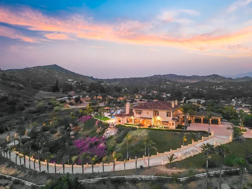 Elevated on a hill in Blossom Valley, this exquisite home offers a living experience that is truly unmatched. Nestled within a gated estate, the property expands across six acres of meticulously landscaped grounds, showcasing natural rock formations and a vibrant variety of palm trees, succulents, and blooming flowers. Embracing eco-friendly features such as a ground-water well and solar panels, this residence seamlessly blends sustainability with luxurious living. 15987 Broad Oaks Road Home in El Cajon, California.