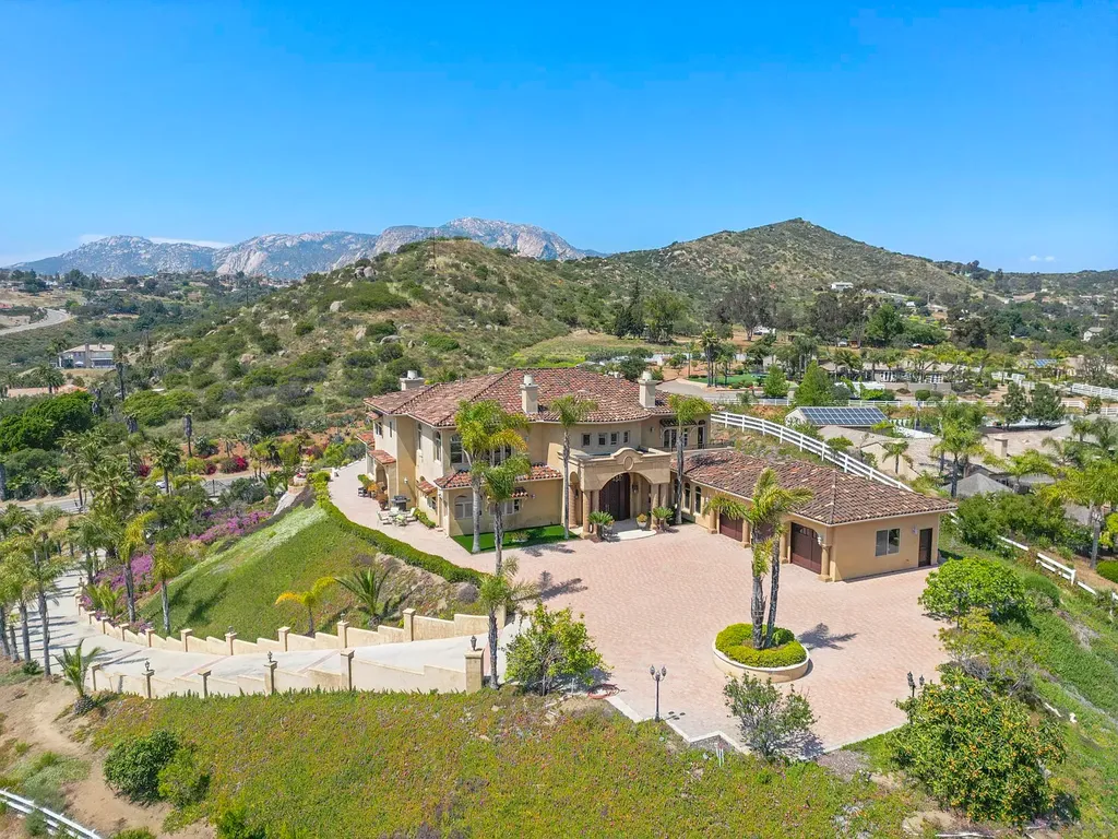 Elevated on a hill in Blossom Valley, this exquisite home offers a living experience that is truly unmatched. Nestled within a gated estate, the property expands across six acres of meticulously landscaped grounds, showcasing natural rock formations and a vibrant variety of palm trees, succulents, and blooming flowers. Embracing eco-friendly features such as a ground-water well and solar panels, this residence seamlessly blends sustainability with luxurious living. 15987 Broad Oaks Road Home in El Cajon, California.