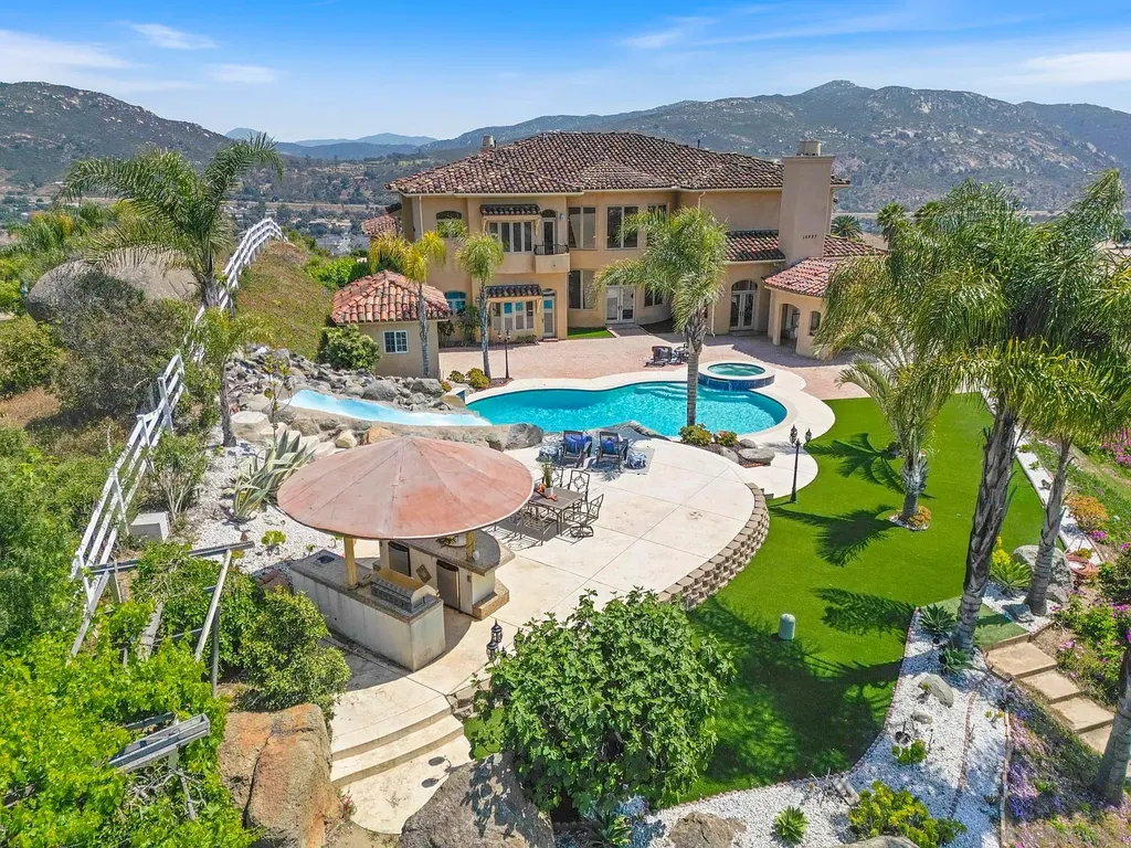 Elevated on a hill in Blossom Valley, this exquisite home offers a living experience that is truly unmatched. Nestled within a gated estate, the property expands across six acres of meticulously landscaped grounds, showcasing natural rock formations and a vibrant variety of palm trees, succulents, and blooming flowers. Embracing eco-friendly features such as a ground-water well and solar panels, this residence seamlessly blends sustainability with luxurious living. 15987 Broad Oaks Road Home in El Cajon, California.