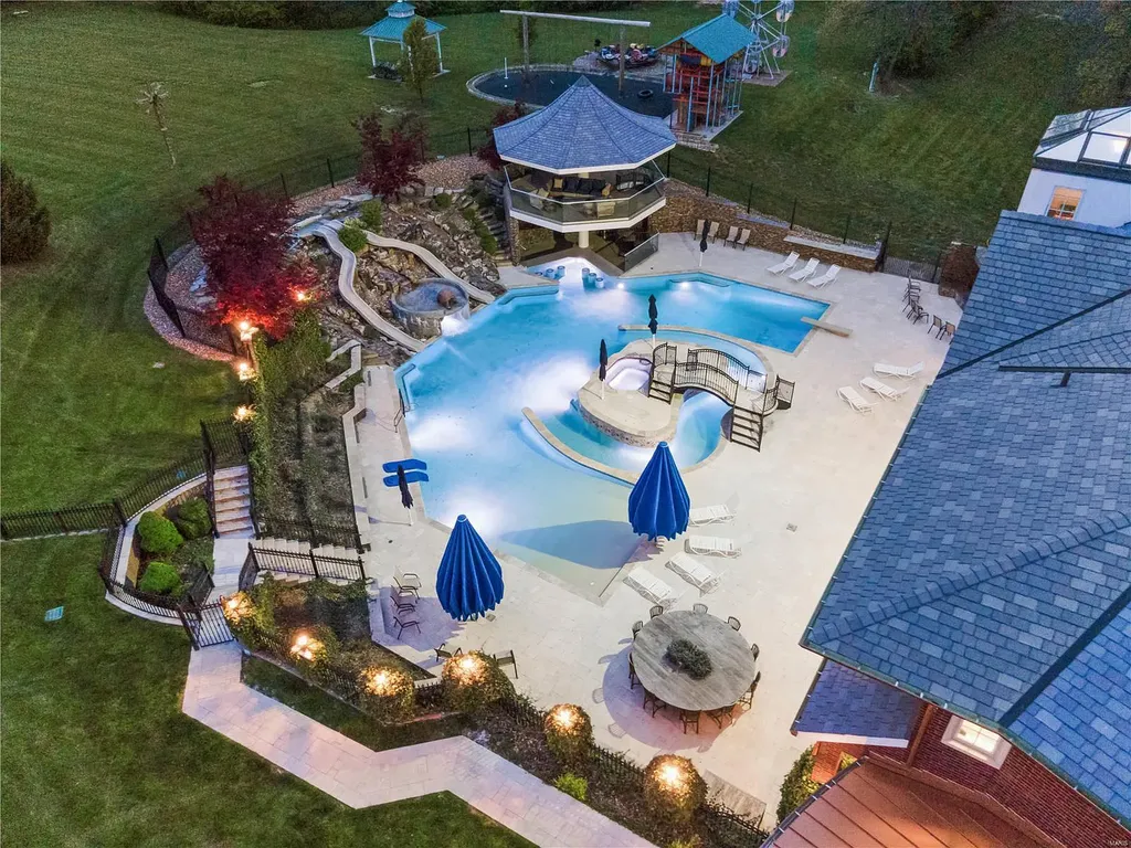 7 Hillside Court Home in Wentzville, Missouri. Prepare for a life-changing experience in this remarkable home that transcends conventional expectations. Embrace the embrace over 20,000 sq. ft. of "Luxury Meant to be Lived In," meticulously designed to cater to multigenerational families, offering abundant space for all. Situated on a vast 20+ acre property (expandable up to 130 acres), this estate presents a plethora of amenities including stables, a sports field, playground, Ferris wheel, event/sports venue, raised bed gardens, and a resort-worthy pool featuring racing slides, a swim-up bar, lazy river, waterfall-covered grotto, dive board, and a zero-edge entry.