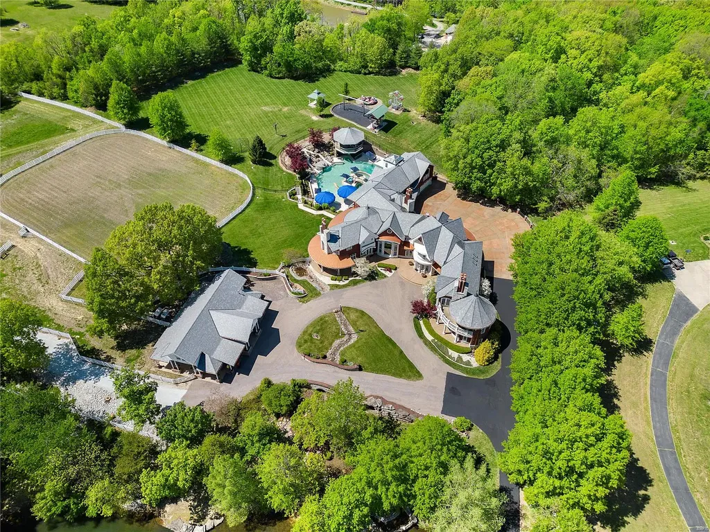 7 Hillside Court Home in Wentzville, Missouri. Prepare for a life-changing experience in this remarkable home that transcends conventional expectations. Embrace the embrace over 20,000 sq. ft. of "Luxury Meant to be Lived In," meticulously designed to cater to multigenerational families, offering abundant space for all. Situated on a vast 20+ acre property (expandable up to 130 acres), this estate presents a plethora of amenities including stables, a sports field, playground, Ferris wheel, event/sports venue, raised bed gardens, and a resort-worthy pool featuring racing slides, a swim-up bar, lazy river, waterfall-covered grotto, dive board, and a zero-edge entry.
