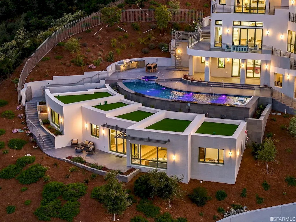165 Woodridge Road Home in Hillsborough, California. Situated on 2.19 acres, this brand new state-of-the-art construction in Northern California boasts unobstructed, panoramic views as far as the eye can see. The architectural marvel features 26-ft high curved ceilings, rounded walls, and floor-to-ceiling windows, bathing the interior in natural light and showcasing breathtaking 180-degree bay and canyon vistas. Step onto the stunning limestone terrace, where a curved pool with a dancing water feature, spa, built-in Kalamazoo bbq station, outdoor shower, and access to a luxurious 2-bedroom, 2-bath guest house await. 
