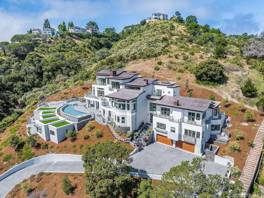 165 Woodridge Road Home in Hillsborough, California. Situated on 2.19 acres, this brand new state-of-the-art construction in Northern California boasts unobstructed, panoramic views as far as the eye can see. The architectural marvel features 26-ft high curved ceilings, rounded walls, and floor-to-ceiling windows, bathing the interior in natural light and showcasing breathtaking 180-degree bay and canyon vistas. Step onto the stunning limestone terrace, where a curved pool with a dancing water feature, spa, built-in Kalamazoo bbq station, outdoor shower, and access to a luxurious 2-bedroom, 2-bath guest house await. 