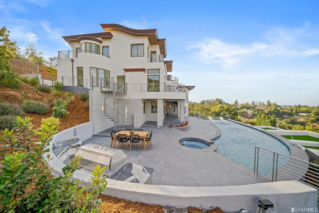 165 Woodridge Road Home in Hillsborough, California. Situated on 2.19 acres, this brand new state-of-the-art construction in Northern California boasts unobstructed, panoramic views as far as the eye can see. The architectural marvel features 26-ft high curved ceilings, rounded walls, and floor-to-ceiling windows, bathing the interior in natural light and showcasing breathtaking 180-degree bay and canyon vistas. Step onto the stunning limestone terrace, where a curved pool with a dancing water feature, spa, built-in Kalamazoo bbq station, outdoor shower, and access to a luxurious 2-bedroom, 2-bath guest house await. 